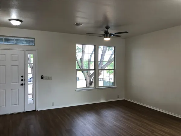 an empty room with wooden floor chandelier fan and windows