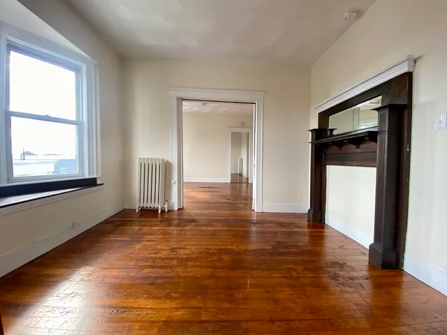 a view of an empty room with window and wooden floor