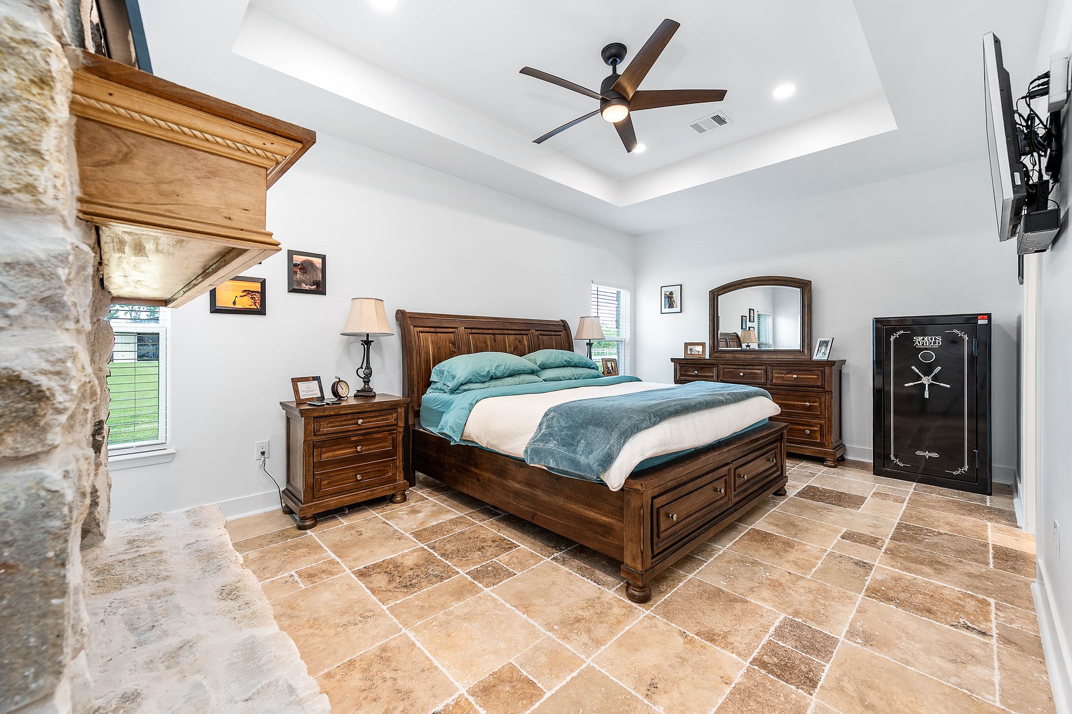 8032 Short Road Needville, TX 77461 - Photo 16 of 50 The Primary bedroom features a stunning stone accent wall, tray ceiling with modern lighting and fan, and large windows that fill the room with natural light. The thoughtful design, warm finishes, and generous layout create a comfortable and relaxing private retreat.