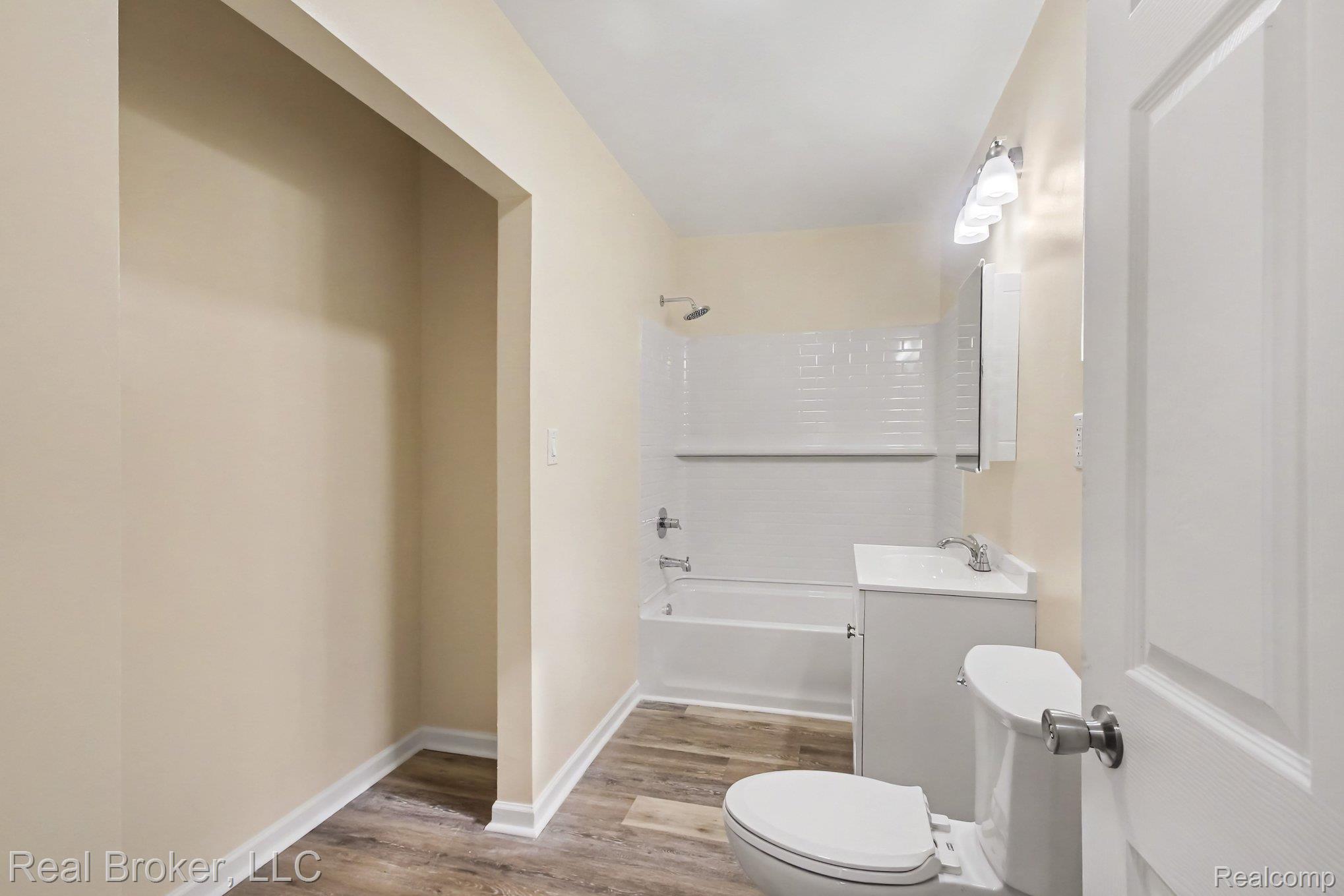 217 East Edgar Bergen Boulevard Decatur, MI 49045 - Photo 11 of 16 Bathroom featuring wood-finish flooring, a white vanity with an integrated sink, a built-in tub with subway tile surround, and a wall-mounted light fixture