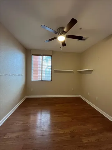 an empty room with wooden floor fan and windows