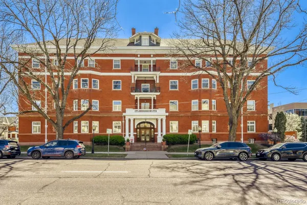 a front view of a building with lot of cars and trees