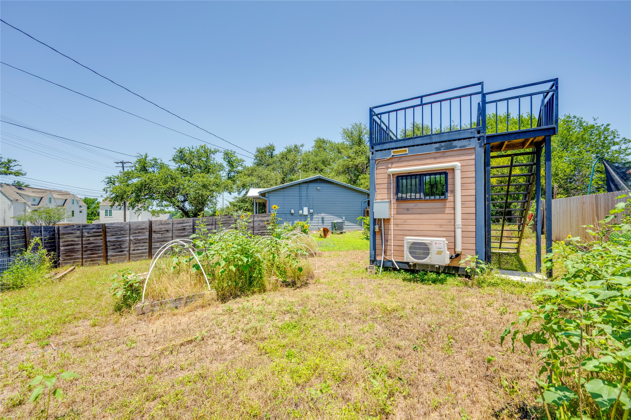 1707 Overhill Drive Austin, TX 78721 - Photo 30 of 36 A unique backyard features a compact structure with an elevated deck, nestled beside a green space with garden beds.