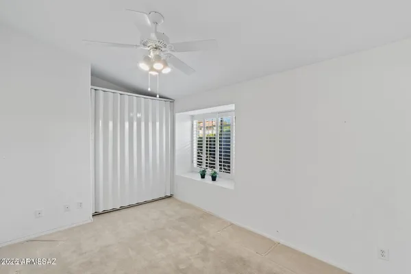 an empty room with chandelier fan and windows