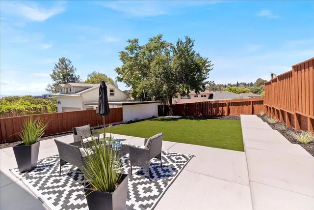 a view of a backyard with table and chairs plants and large tree