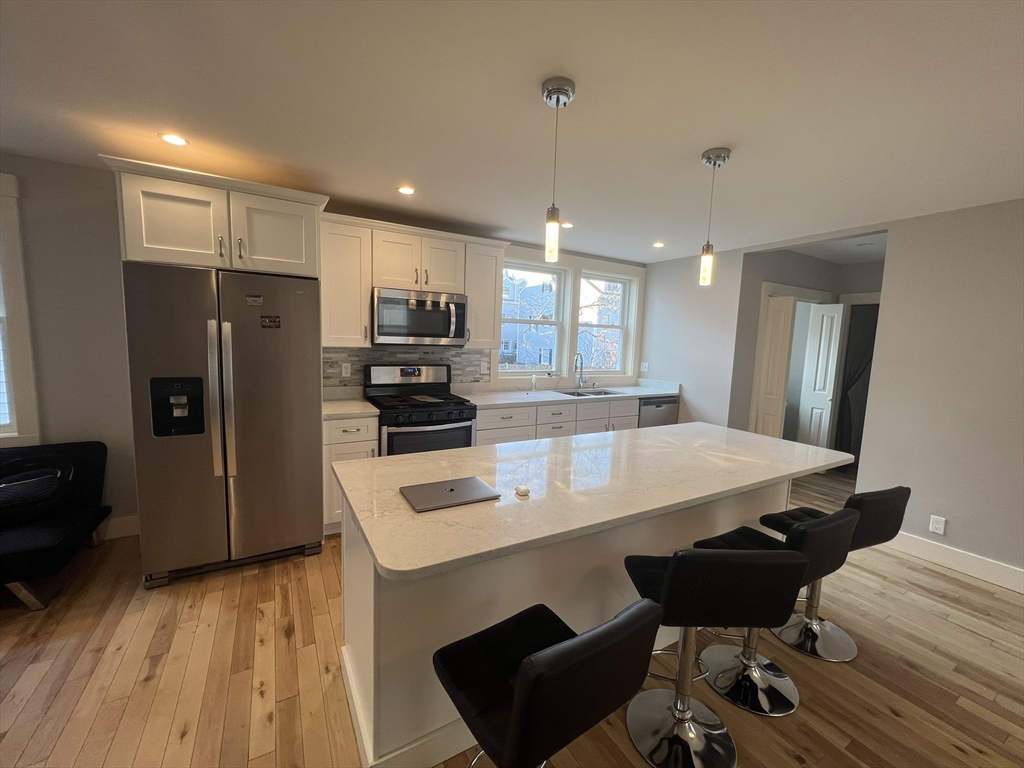 39 Snow Street, Unit 1 Boston, MA 02135 - Photo 9 of 35 a kitchen with stainless steel appliances kitchen island granite countertop a refrigerator a stove and a wooden floor
