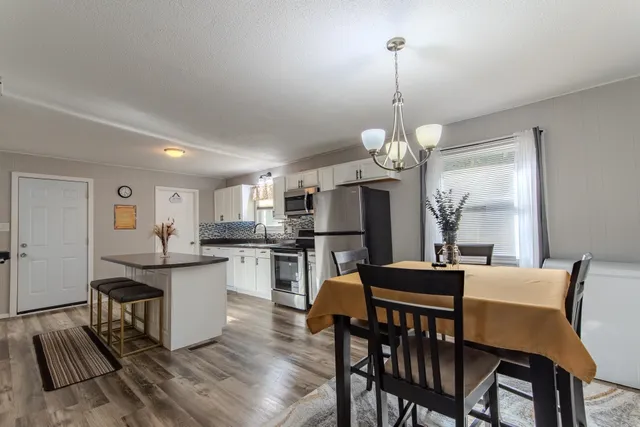 a kitchen with stainless steel appliances kitchen island granite countertop a dining table chairs and a refrigerator