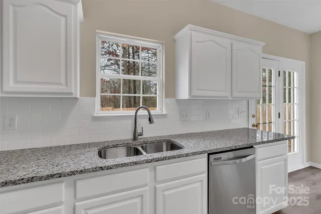 a kitchen with stainless steel appliances granite countertop a sink a refrigerator and white cabinets