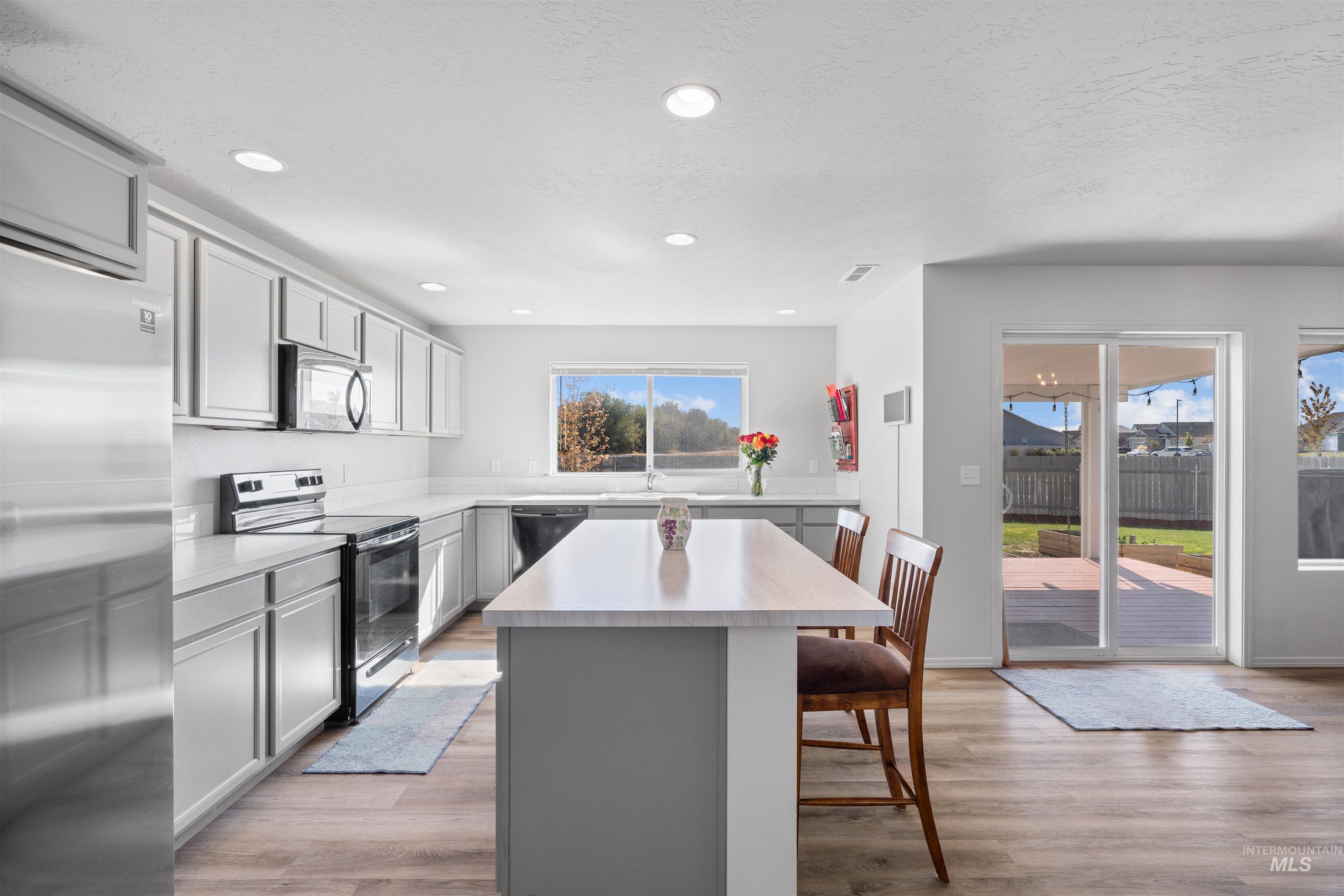 12731 Sondra Street Caldwell, ID 83607 - Photo 13 of 46 Kitchen featuring a center island, gray cabinets, black appliances, light countertops, and light wood-style floors