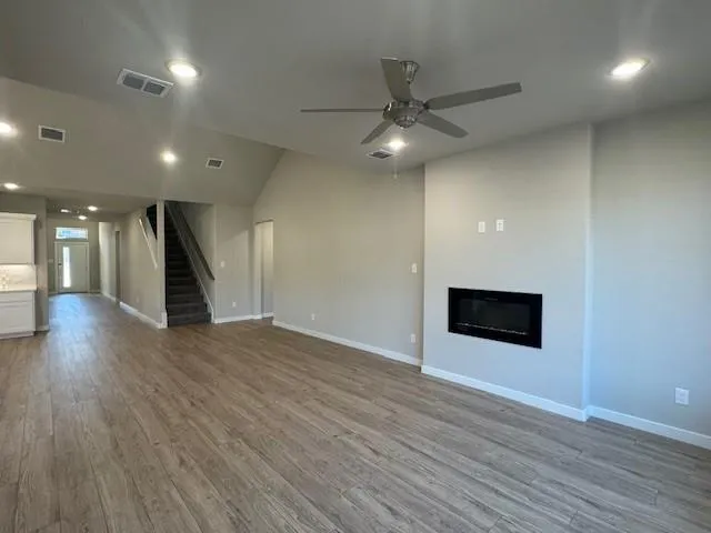 a view of an empty room with wooden floor and a ceiling fan