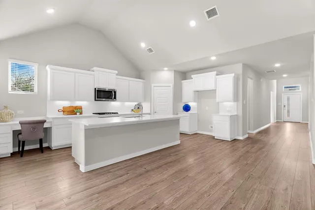 a large white kitchen with white cabinets a sink dishwasher a dining table and chairs with wooden floor