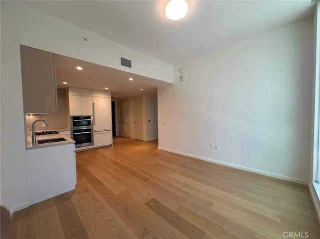 an empty room with wooden floor and a kitchen