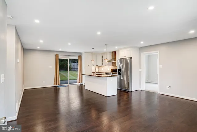 a view of large kitchen with stainless steel appliances granite countertop a refrigerator a sink a stove and oven with wooden floor