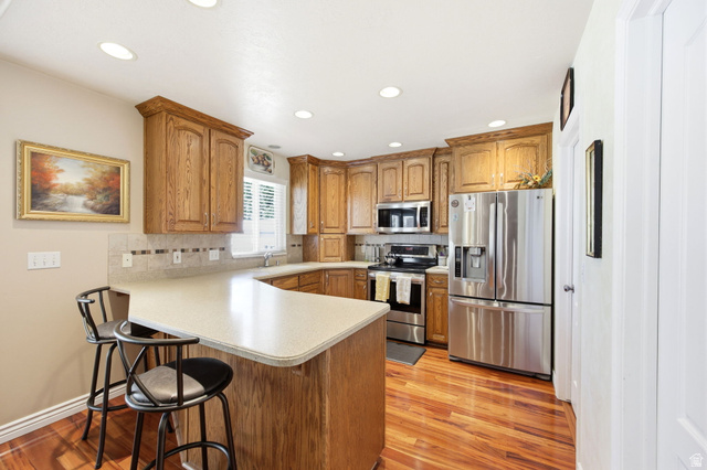 776 Flint Street Layton, UT 84041 - Photo 4 of 41 Kitchen featuring wood cabinetry, stainless steel appliances, a light-toned countertop, tile backsplash, and wood-finish flooring