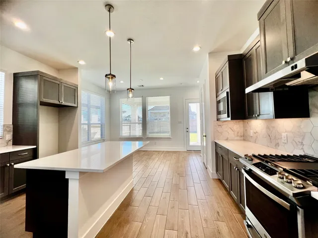 a large kitchen with stainless steel appliances a stove a sink dishwasher and a refrigerator with wooden floor