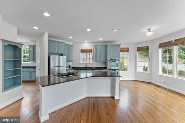 a kitchen with stainless steel appliances granite countertop a sink a stove a refrigerator and island with wooden floor