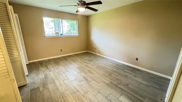 an empty room with wooden floor fan and windows