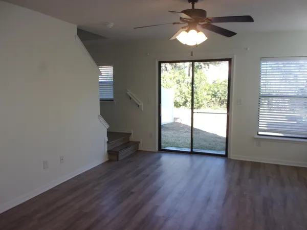 a view of an empty room with wooden floor and a ceiling fan