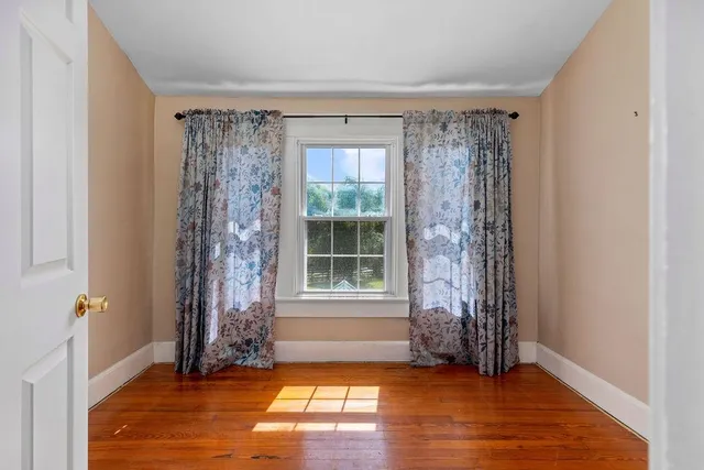 an empty room with wooden floor chandelier and windows