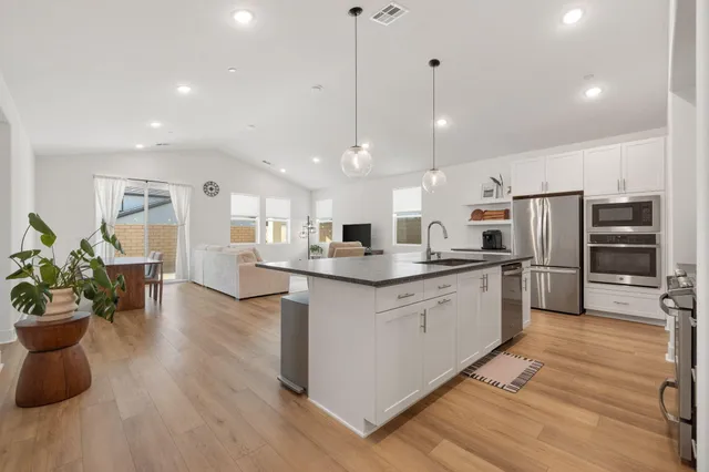 a kitchen with stainless steel appliances kitchen island granite countertop a refrigerator a stove a sink dishwasher and a dining table with wooden floor
