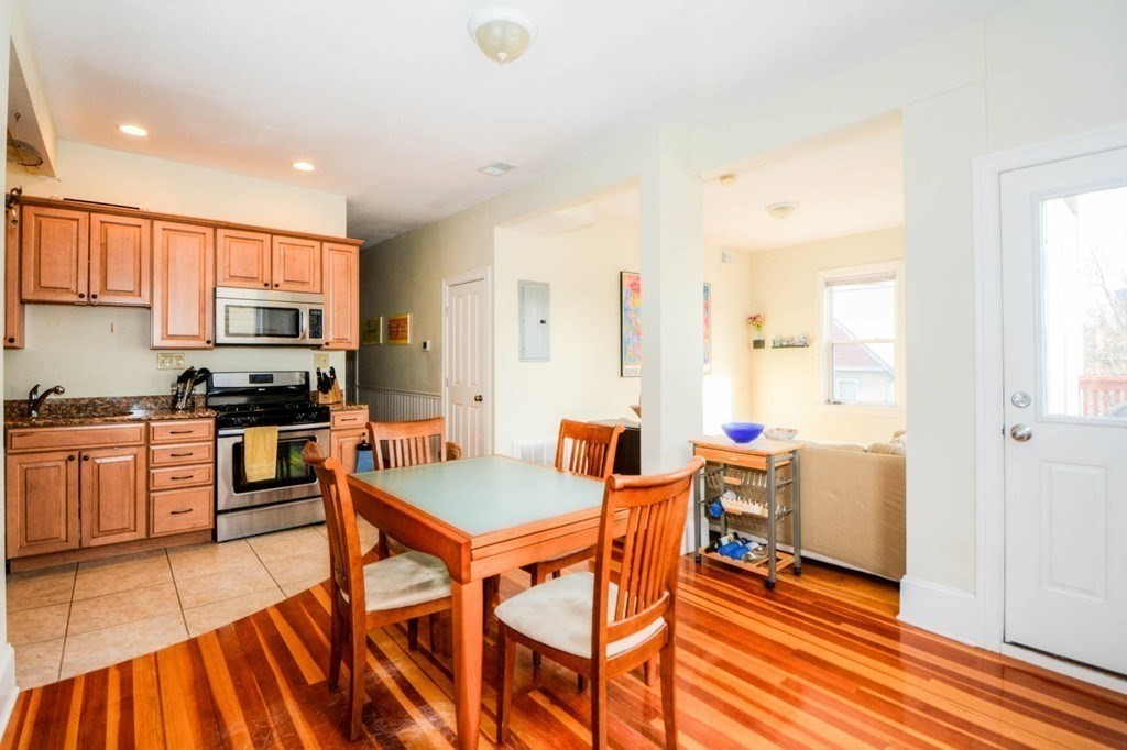 137 Paul Gore Street, Unit 2 Boston, MA 02130 - Photo 2 of 11 a kitchen with stainless steel appliances granite countertop a stove top oven a sink a dining table and chairs with wooden floor