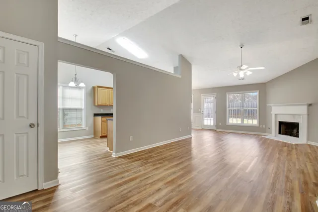 a view of an empty room with wooden floor fireplace and a window
