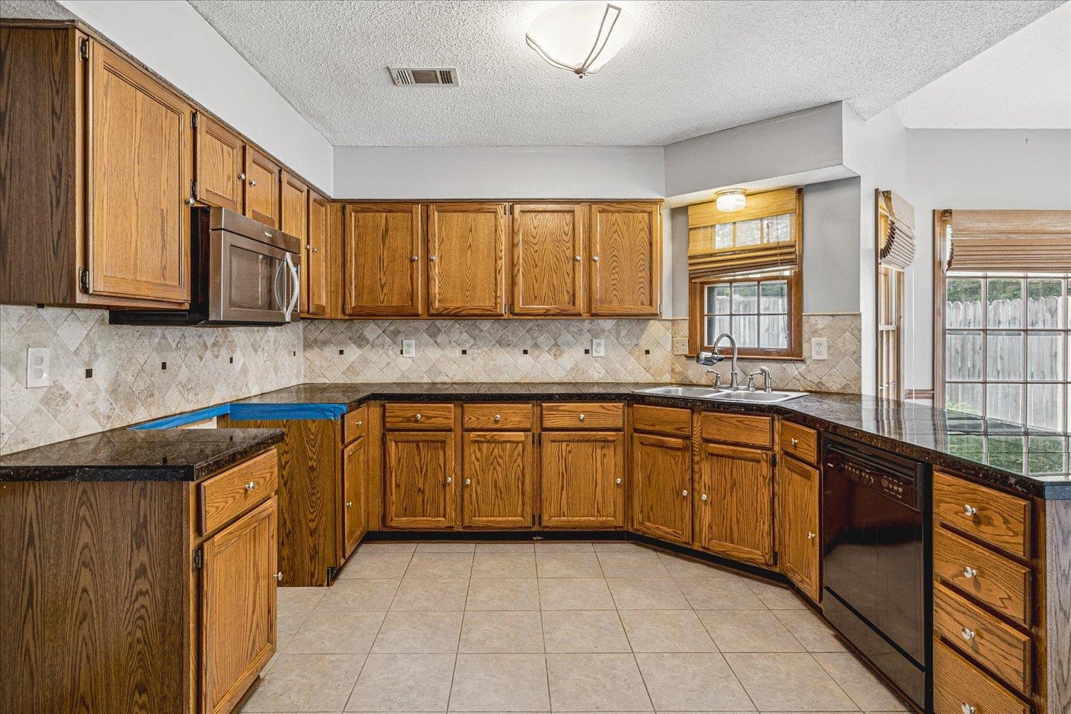 8529 Buckhurst Road Memphis, TN 38016 - Photo 13 of 36 Kitchen with wood finish cabinetry, black dishwasher, light tile patterned flooring, stainless steel microwave, and a textured ceiling