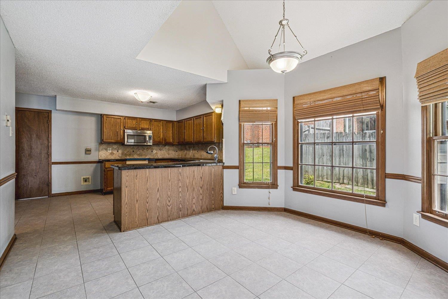 8529 Buckhurst Road Memphis, TN 38016 - Photo 17 of 36 Kitchen with wood finish cabinets, decorative backsplash, pendant lighting, a peninsula, and stainless steel microwave