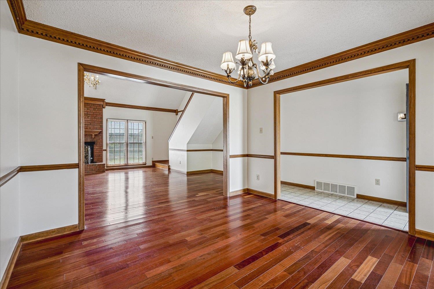 8529 Buckhurst Road Memphis, TN 38016 - Photo 7 of 36 Empty room featuring crown molding, hardwood / wood-style flooring, a chandelier, a fireplace, and a textured ceiling