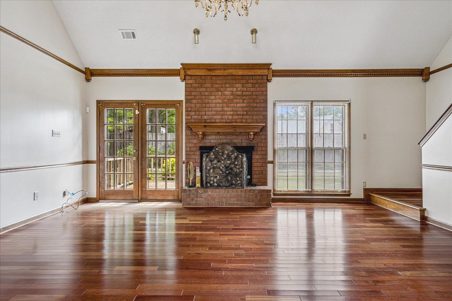 8529 Buckhurst Road Memphis, TN 38016 - Photo 9 of 36 Unfurnished living room with lofted ceiling, a brick fireplace, hardwood / wood-style flooring, ornamental molding, and a chandelier
