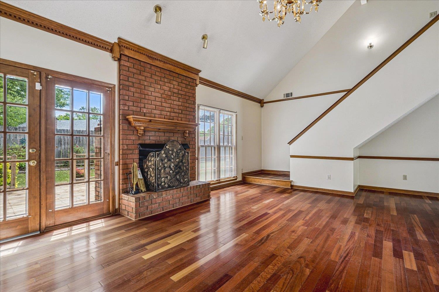 8529 Buckhurst Road Memphis, TN 38016 - Photo 10 of 36 Unfurnished living room featuring wood-type flooring, a brick fireplace, crown molding, lofted ceiling, and suspended lighting