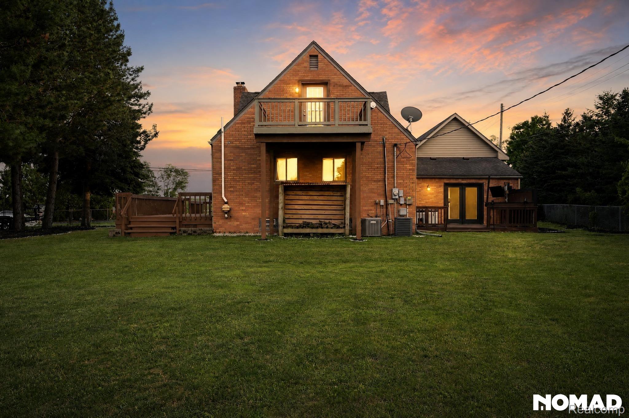 8315 Hilton Road Brighton, MI 48114 - Photo 1 of 26 Expansive green lawn with a red brick exterior featuring a second-story balcony and two ground-level wood decks