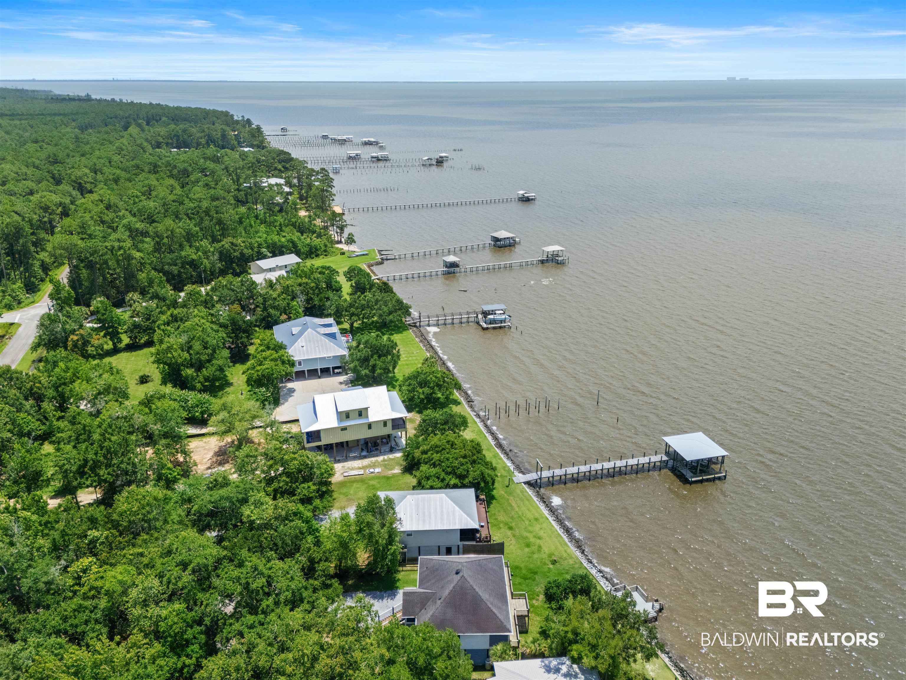 9581 South Bay Street Foley, AL 36535 - Photo 40 of 44 Coastal property featuring a waterfront setting, private dock with covered boat lift, extensive tree coverage, and an elevated residence with a light-colored exterior