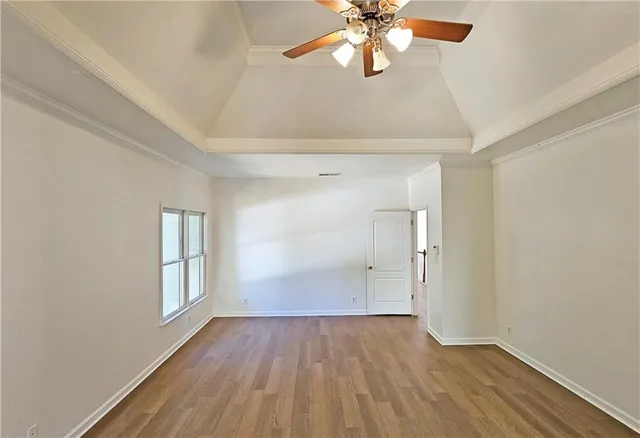 an empty room with wooden floor chandelier fan and windows