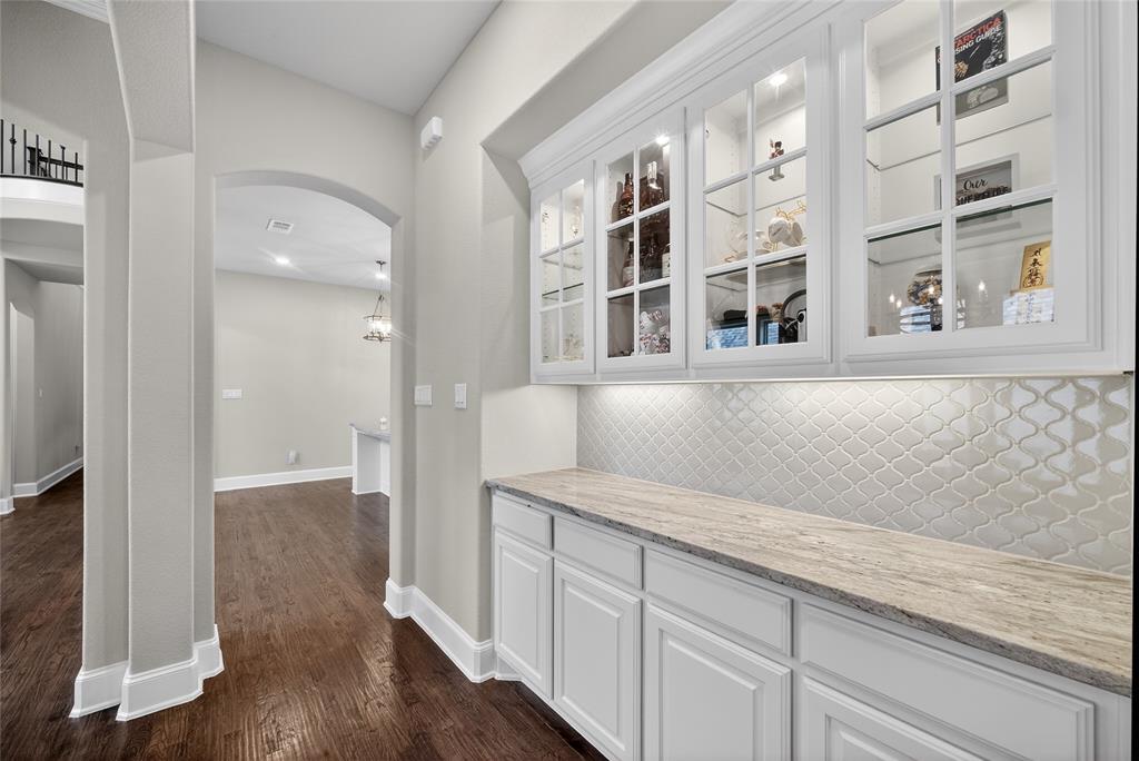 1039 Stephen Street Allen, TX 75013 - Photo 17 of 40 Bar featuring glass fronted cabinets, arched walkways, white cabinetry, light stone countertops, and dark wood-style floors