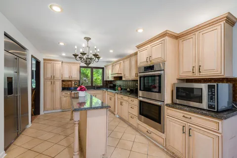 a kitchen with stainless steel appliances kitchen island granite countertop a refrigerator oven a sink dishwasher and white cabinets with wooden floor