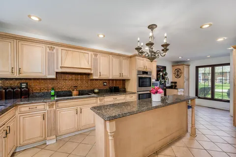 a kitchen with kitchen island granite countertop a stove a sink a oven and a white cabinets