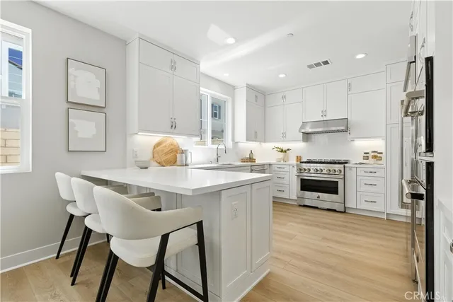 a kitchen with stainless steel appliances granite countertop a stove a refrigerator a kitchen island and chairs with wooden floor