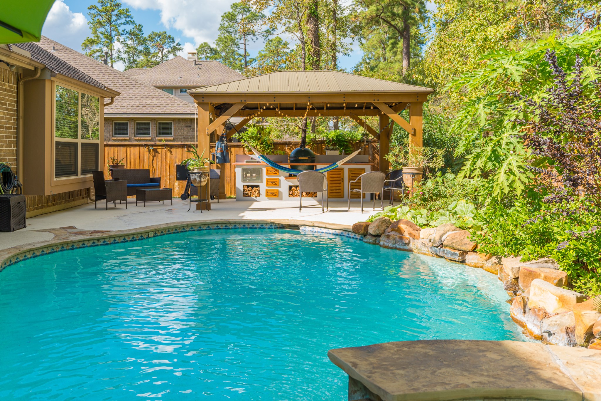 30 Fury Ranch Place The Woodlands, TX 77375 - Photo 45 of 47 This backyard showcases a beautiful swimming pool surrounded by lush greenery and a stone border. Adjacent is a spacious patio with comfortable seating and a stylish gazebo, perfect for relaxation and entertaining. The area provides a serene, resort-like atmosphere.