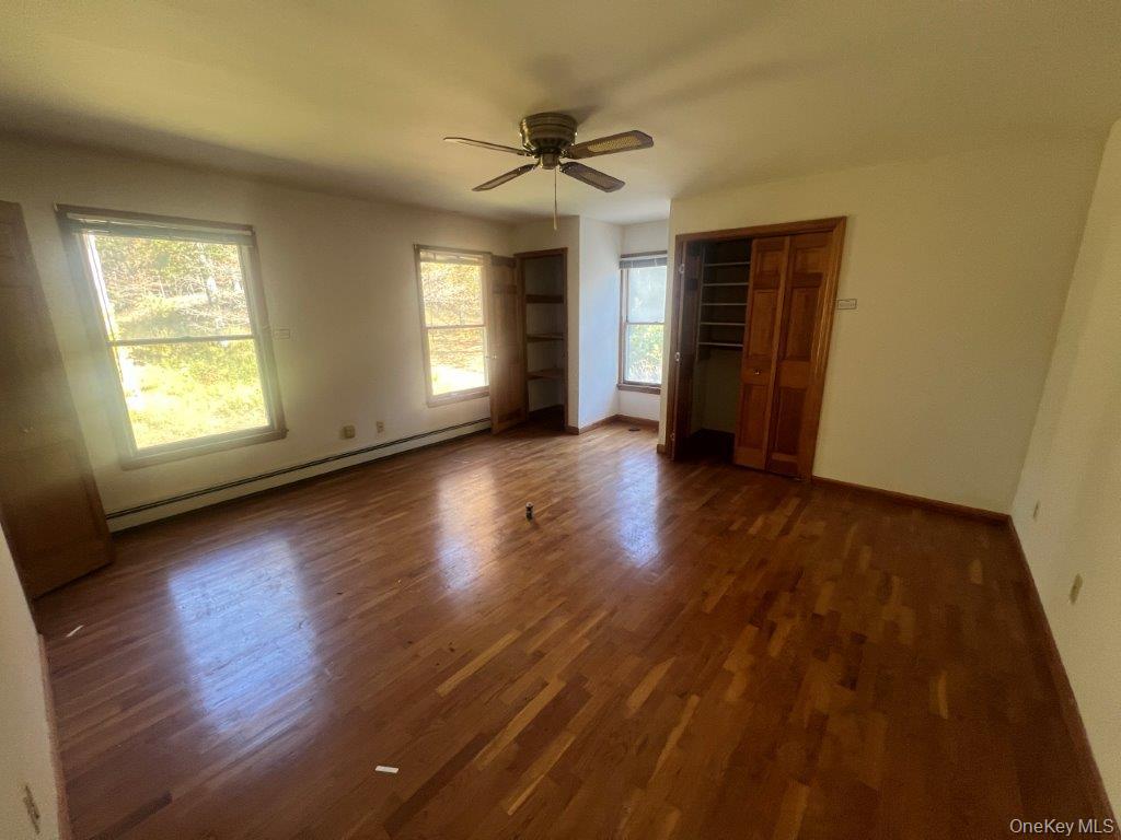 7 Felter Hill Road Monroe, NY 10950 - Photo 12 of 12 Unfurnished bedroom featuring a baseboard radiator, dark wood finished floors, ceiling fan, and two closets
