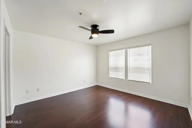 an empty room with wooden floor ceiling fan and windows
