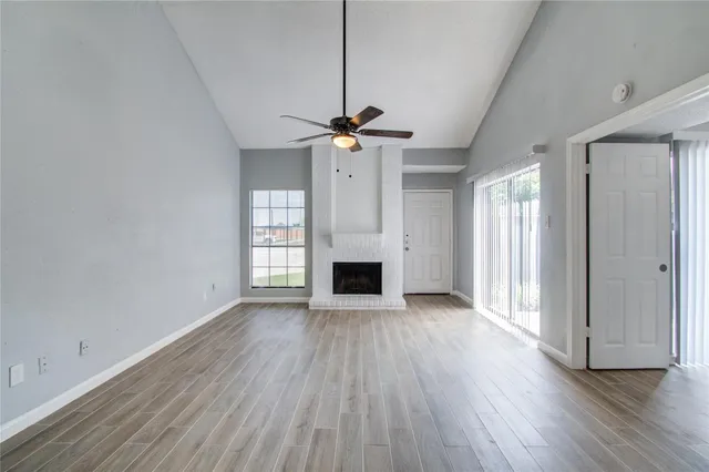 an empty room with wooden floor a ceiling fan a fireplace and windows