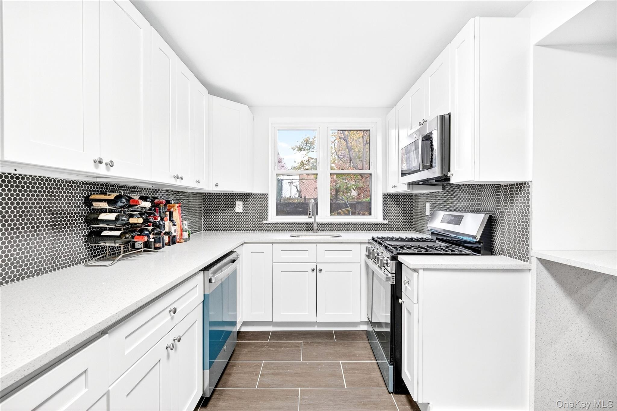 1458 Rowland Street Bronx, NY 10461 - Photo 7 of 49 Kitchen featuring white cabinetry, appliances with stainless steel finishes, decorative backsplash, light stone counters, and light tile patterned flooring