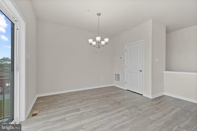 a view of a chandelier in big room with wooden floor and a window