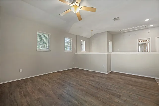 a view of an empty room with wooden floor and a ceiling fan