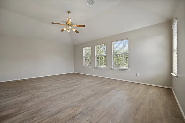 an empty room with wooden floor fan and windows