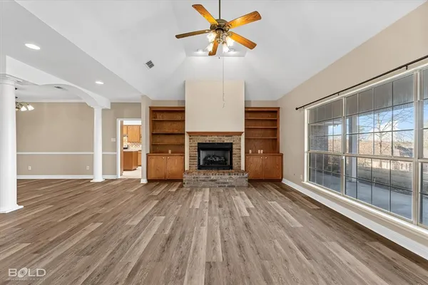 a view of a livingroom with a fireplace a ceiling fan and windows