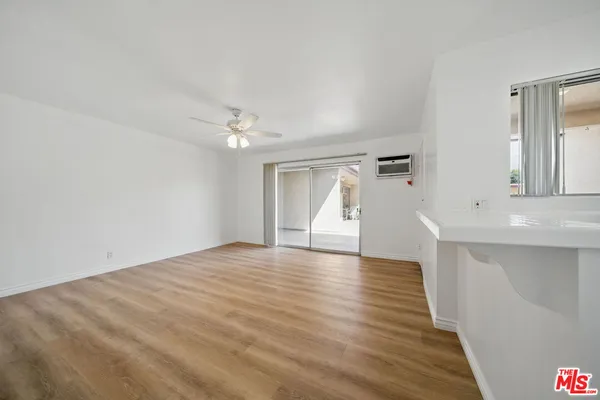 a view of an empty room with wooden floor and a kitchen