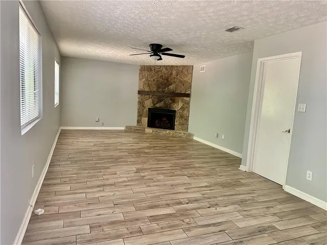 a view of an empty room with wooden floor fireplace and a window
