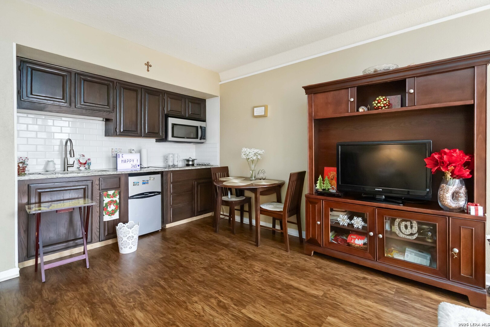 a living room with stainless steel appliances furniture a fireplace a flat screen tv and kitchen view
